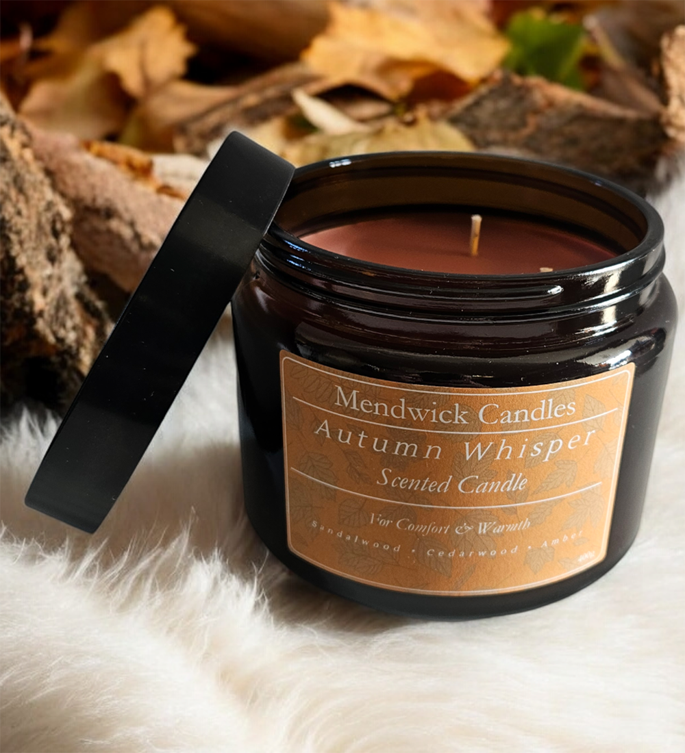 Mendwick Candles Autumn Whisper scented candle shown on top of cashmere with leaves and logs in the background