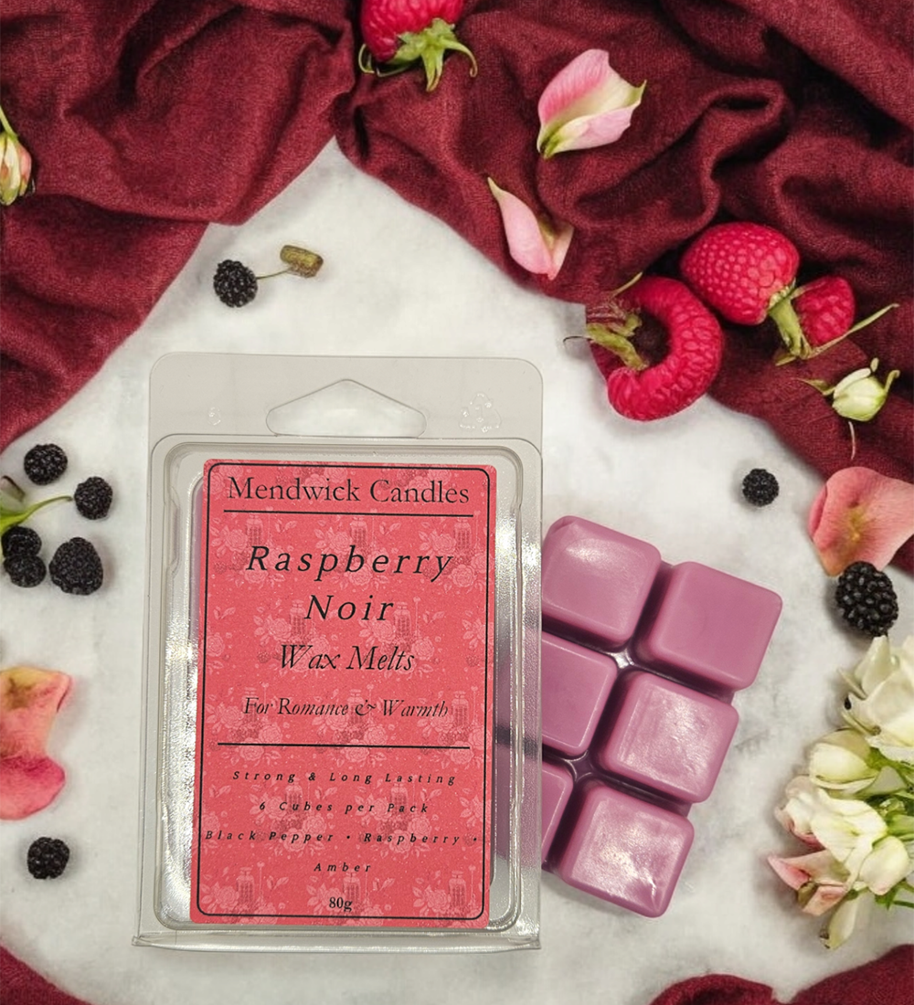 Raspberry Noir wax melts surrounded by soft red fabric, raspberries, black berries and petals 